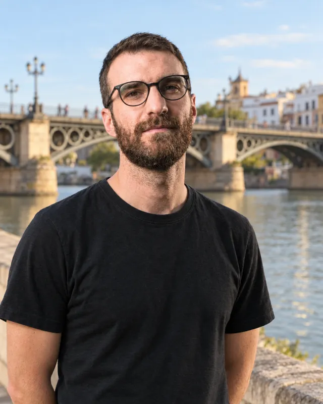 Portrait of Carlos Requena, wearing glasses and a black T-shirt, with Seville’s Triana bridge behind him.